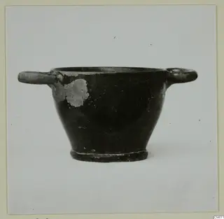 Black-glazed pottery bowl with two horizontal handles, photographed against a plain background.