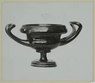 Black-glazed pottery bowl with two horizontal handles and a low foot, photographed against a plain background.