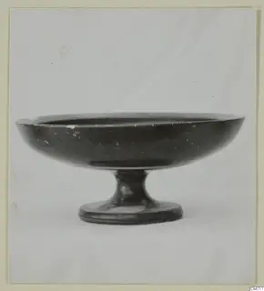 Black-glazed pedestal bowl with a wide, shallow bowl on a short stem and round foot, photographed against a plain background.