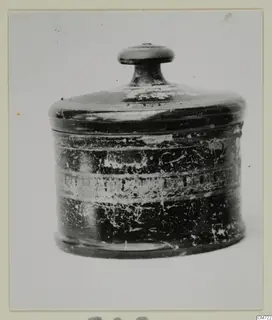Lidded cylindrical pottery vessel with a knob handle on its lid and a worn dark surface with pale bands