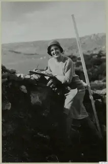 Ebba Elgenstierna seated on a stone wall at Nitovikla, writing in a notebook, with a measuring pole beside her.