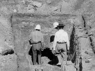 Three men seen from behind walking into a dark tomb opening at Stylli