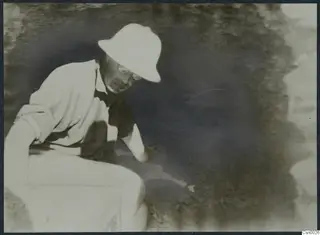 Crown Prince Gustav Adolf in a pith helmet and glasses, bending down to dig at Stylli.