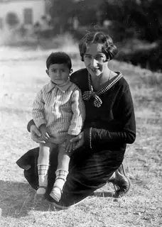 Rosa Lindros crouching outdoors at Lapithos with a small boy on her lap, both looking at the camera.