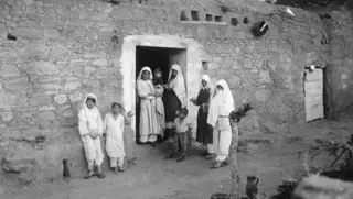 Women, children and a baby at the doorway of a stone house with a whitewashed frame, in the Karpas peninsula