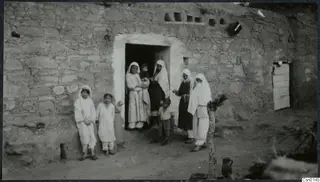 Women, children and a small boy grouped at the doorway of a stone house, probably a village in the Karpas peninsula