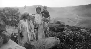 Children standing among stones on a hillside, with a fallen column drum in the foreground.