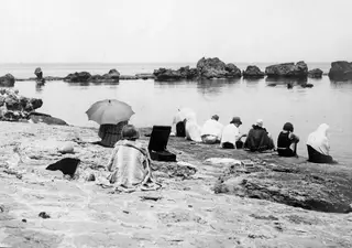 Expedition members sitting on a rocky shelf by the sea below Vouni