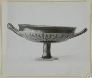 Black-glazed bowl on a tall foot, with two horizontal handles and a band of leaf-like motifs below the rim