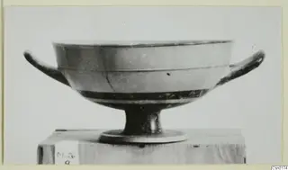 Two-handled footed bowl with dark glaze bands, shown in side view on a wooden block.