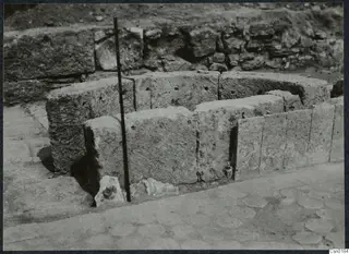 Curved stone wall of large dressed blocks at Salamis, with a dark measuring rod standing beside it