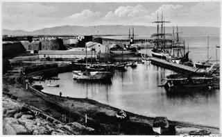 Harbour at Salamis near Famagusta, with moored boats, masted sailing ships, a jetty and a stone fortification wall.