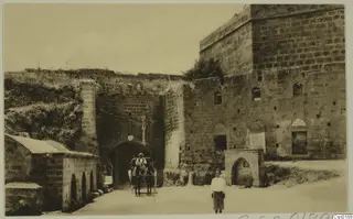Stone gateway with a horse-drawn carriage passing through its arch, and a boy standing in the road in front.