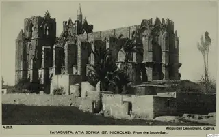 Ruined Ayia Sophia (St. Nicholas) church in Famagusta seen from the south-east, with palm trees and a low wall in front.