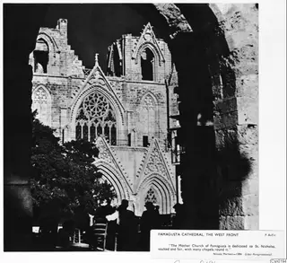 West front of Famagusta cathedral, a ruined church with pointed arches and a rose window, seen through a stone arch