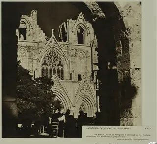 West front of Famagusta cathedral with a round window, seen past a tree and silhouetted people.