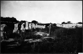 Ruined stone walls at Salamis with a man in a suit and hat standing among overgrown grass