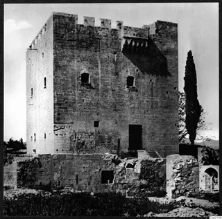 Kolossi castle, a tall square stone tower with battlements, with a cypress tree beside it