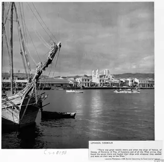 Limassol harbour with a moored sailing ship in the foreground, waterfront buildings and a twin-towered church beyond.
