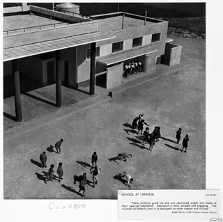 Children in a schoolyard at Limassol beside a two-storey building with tall round columns, seen from above