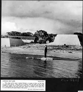 Larnaca salt lake with pale walls of salt pans along the shore and a man standing at the water's edge