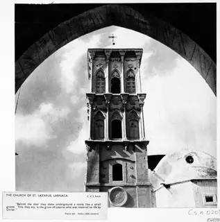 Stone tower of the Church of St. Lazarus, Larnaca, seen through a dark arched frame, with a cross on its top