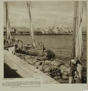 Limassol harbour with sacks stacked on the quay beside moored sailing boats and a domed church behind the waterfront.