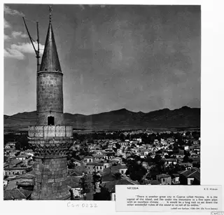 Nicosia seen from above: a tall stone tower with a conical top, rows of houses and distant mountains.