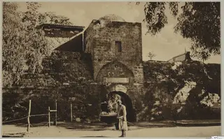 Stone gateway with a domed tower in Nicosia, with a standing man in light robes and trees on either side
