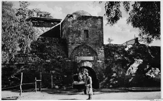 Stone gateway with a domed tower in the city wall at Nicosia, with a standing man in light clothing in front.
