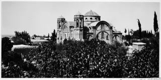 Domed church with two bell towers behind dense shrubs and cypress trees, Nicosia