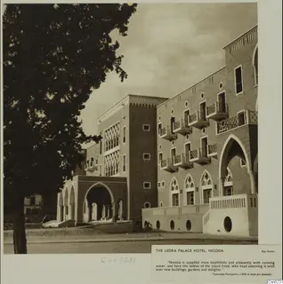 Ledra Palace Hotel, Nicosia, with arched openings and balconies, seen beside a large tree in the foreground.