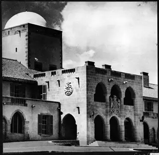 Stone building in Nicosia with arched openings, a carved relief panel, a domed tower behind and a flight of steps at right
