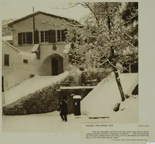 Snowy street at the Paphos Gate, Nicosia, with an arched gateway, a snow-laden tree and one person walking in the snow.