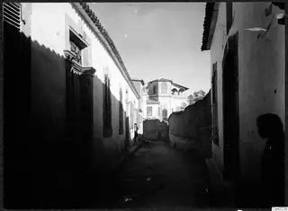 Narrow street in Nicosia lined with whitewashed buildings and shuttered windows, with a dog and a standing person