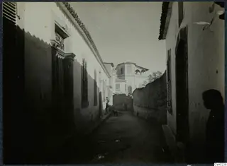 Narrow street in Nicosia lined with whitewashed buildings, with a dog and a person near the left wall