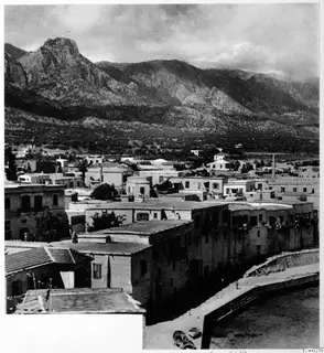Town of Kyrenia seen from above, with flat-roofed houses, a harbour quay and a mountain range behind