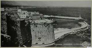 Kyrenia harbour with a round stone fort tower, white buildings, a sailing boat and the open sea.