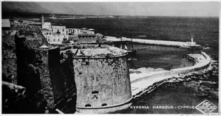Kyrenia harbour with a round stone tower, a two-masted sailing boat and a breakwater ending in a lighthouse