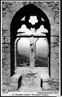 Pointed stone window with carved tracery in a castle wall, framing a view of hills.