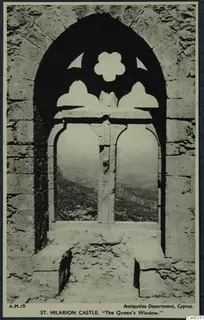 Pointed stone window with carved tracery, looking out over hills and scrubby vegetation in the Kyrenia Mountains.