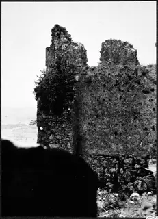 Ruined stone wall with a shrub growing from its face, with a hazy open landscape beyond it in the Kyrenia Mountains
