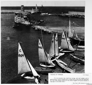 Small numbered sailing dinghies drawn up on the quay at Kyrenia harbour, with a ruined stone tower and breakwater behind.