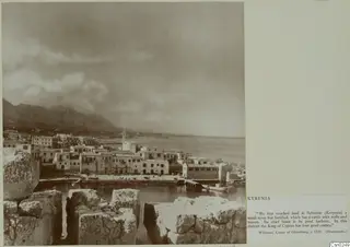 Kyrenia harbour and waterfront houses seen over ancient stone blocks, with mountains and sea beyond.