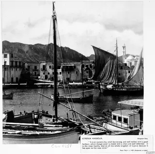 Kytenia harbour with moored boats and sails, waterfront houses and hills behind