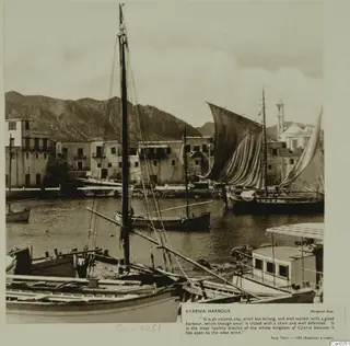 Kyrenia harbour with moored wooden boats, tall masts and whitewashed waterfront houses behind the water