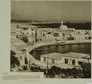 Harbour at Kyrenia with white houses along the curved quay and small boats moored in the water