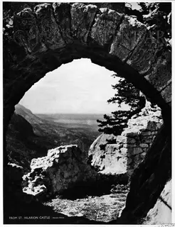 View through a stone arch over a hazy valley and mountains, with a pine tree and broken stone walls beside it