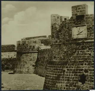 Thick stone fortification wall with square towers and a carved relief panel set into one tower face