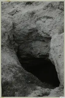 Dark opening cut into a pale earth and rock bank, with grass at its base, at Nicosia